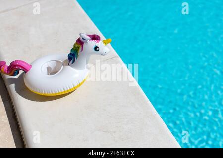 Aufblasbares pinkes Mini-Regenbogen-Einhorn, Cocktail-Stand in der Nähe von Schwimmbad an hellen sonnigen Tag, Kopierraum. Konzept Sommerurlaub, Unterhaltung, Wasser Stockfoto