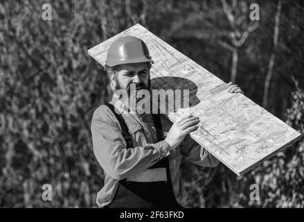 Gerüst einrichten. Provisorische Ausrüstung oder Strukturen montieren. Renovierungsservice. Mann trägt Faserplatte. Holzwerkstoff. Verwendete Faserplatte in Stockfoto