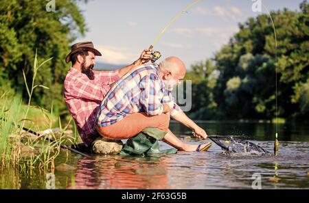 Männer sitzen am Flussufer mit Angelausrüstung. Wilderei Kriminalität und Angelschein. Wilderer, die fischen. Schwarzmarkt Kaviar. Illegale Jagd Kaviar Stockfoto
