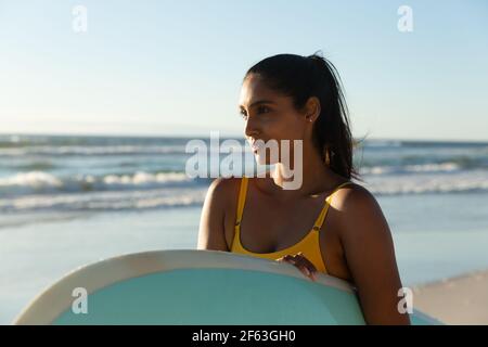 Glückliche Mischrennerin mit Surfbrett am Strand Stockfoto