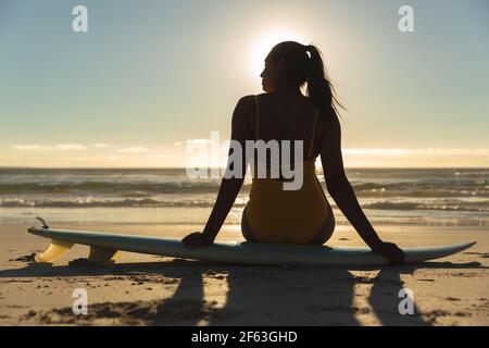 Frau mit gemischter Rasse, die am Strand auf dem Surfbrett sitzt Stockfoto
