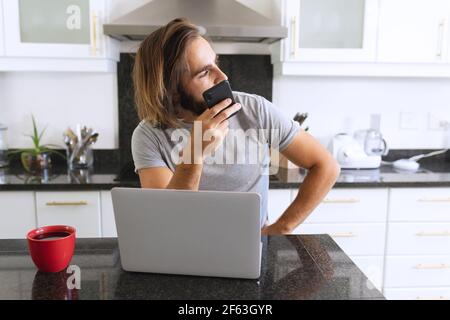 Kaukasischer Mann sitzt in der Küche mit Laptop und Smartphone Stockfoto