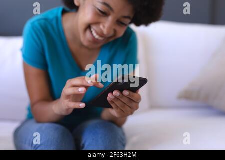 afroamerikanische Frau, die mit dem Smartphone auf dem Sofa sitzt Stockfoto