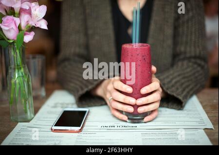 Weibliche Hände halten roten Beerenmoothie im Restaurant. Gesundes Lifestyle-Konzept. London, Großbritannien Stockfoto