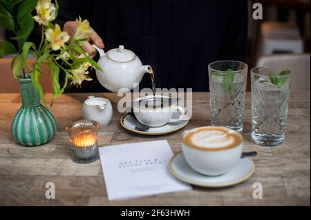 Weibliche Hand gießt Tee aus einer Teekannen im Restaurant. Lifestyle, Afternoon-Tea-Konzept. Leeres Papiermenü mit Kopierbereich. London, Großbritannien Stockfoto