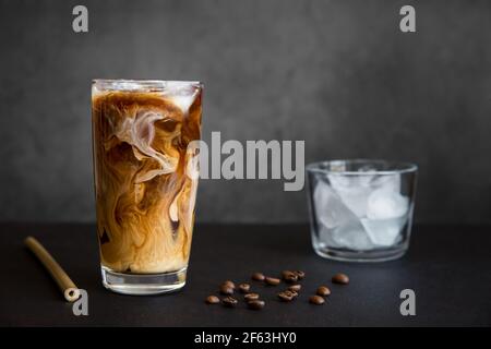 Eiskaffee im hohen Glas mit Sahne, Behälter mit Eis, Cocktailstroh und Kaffeebohnen auf dunklem Hintergrund mit Kopierfläche. Erfrischendes Getränk. Stockfoto