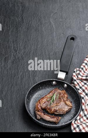Lammkoteletts in Bratpfanne auf schwarzem Stein Hintergrund Stockfoto