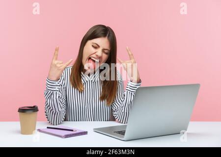 Positive freche Frau blogger zeigt Rock and Roll Finger Geste Blick auf Laptop-Display, chatten Web-Kamera sitzen am Arbeitsplatz. Studio im Innenbereich Stockfoto