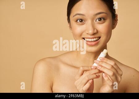 Porträt von schönen jungen Frau lächelnd, während Lippenbalsam, posiert isoliert über beige Hintergrund Stockfoto