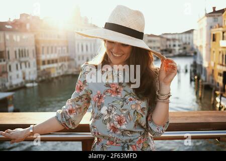 Happy stylish solo Tourist Frau in floralen Kleid mit Hut auf Accademia Brücke in Venedig, Italien. Stockfoto