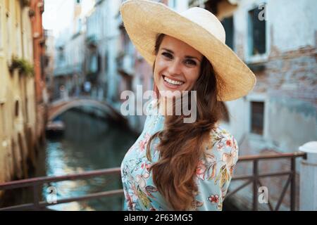 Portrait von lächelnden trendigen Solo-Tourist Frau in floralen Kleid mit Hut genießen Promenade in Venedig, Italien. Stockfoto