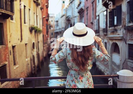 Von hinten gesehen moderne Reisende Frau im mittleren Alter in Blumenkleid mit Hut Sightseeing in Venedig, Italien. Stockfoto