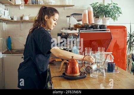 Barista gibt dem Gast im trendigen Café Ordnung. Wasser in Glas gießen Stockfoto
