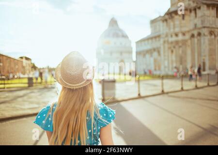 Von hinten gesehen trendy Mädchen in blau insgesamt und Hut mit Ausflug in der Nähe der Kathedrale von Pisa. Stockfoto