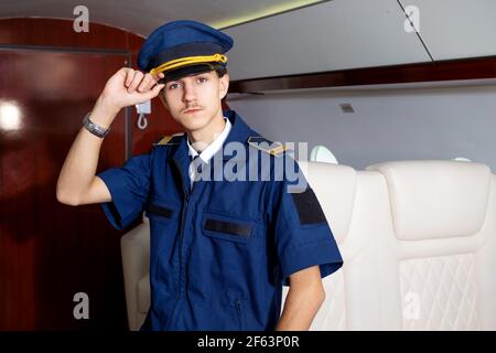 Pilot an Bord des Flugzeugs, die Kabine eines Privatflugzeugs, fliegt mit Komfort. Junger Mann mit Mütze, Crew-Mitglied. Stockfoto