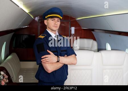 Pilot an Bord des Flugzeugs, die Kabine eines Privatflugzeugs, fliegt mit Komfort. Junger Mann mit Mütze, Crew-Mitglied. Stockfoto
