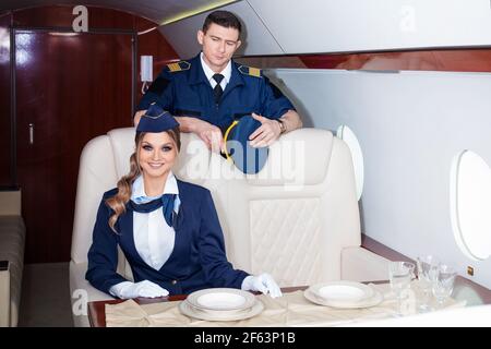 Eine junge Frau, ein Mitglied der Flugzeugcrew an Bord eines Privatjets, begrüßt an Bord des Flugzeugs eine uniformierte Flugbegleiterin. Stockfoto