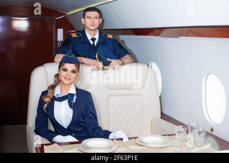 Pilot und ein Flugbegleiter an Bord des Flugzeugs, die Kabine eines Privatflugzeugs, ein Flug mit Komfort. Ein junger Mann und eine Frau in Uniform. Stockfoto