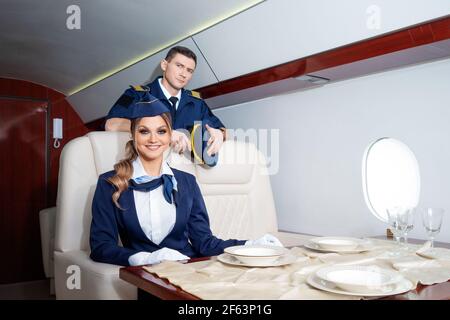 Pilot und ein Flugbegleiter an Bord des Flugzeugs, die Kabine eines Privatflugzeugs, ein Flug mit Komfort. Ein junger Mann und eine Frau in Uniform. Stockfoto