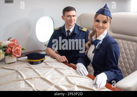 Pilot und ein Flugbegleiter an Bord des Flugzeugs, die Kabine eines Privatflugzeugs, ein Flug mit Komfort. Ein junger Mann und eine Frau in Uniform. Stockfoto