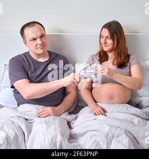 Mann gibt Geld in uns Dollar im Bett für schwangere Frau Stockfoto