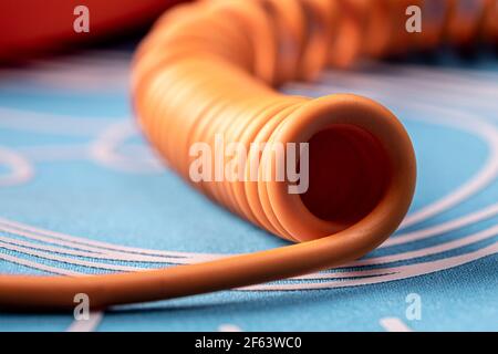 Verdrehtes orangefarbenes Telefonkabel auf blauem Hintergrund. Nahaufnahme mit geringer Schärfentiefe. Stockfoto