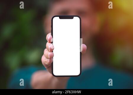Modernes Smartphone-Modell, leerer Bildschirm. Junger Mann zeigt oder hält sein Telefon mit leerem Raum im Freien Stockfoto