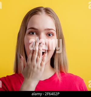 Die junge Frau ist angenehm überrascht. Teenage blonde Mädchen bedeckt ihren offenen Mund mit Hand in Überraschung. Positive emotionale Porträt Frau isoliert auf c Stockfoto