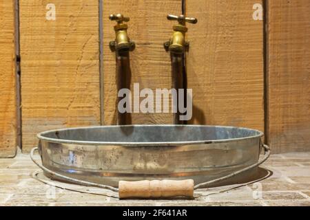 Galvanisiertes Metall Eimer Waschbecken mit rustikalen Messing farbigen Gusseisen Wasserhähne auf Pflasterstein Arbeitsplatte von Holz Waschtisch in Spielzimmer im Keller Stockfoto