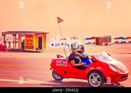 Touristen fahren ein Scoot Coupe Dreirad-Motorrad am Biloxi Beach, 27. März 2021, in Biloxi, Mississippi. Stockfoto