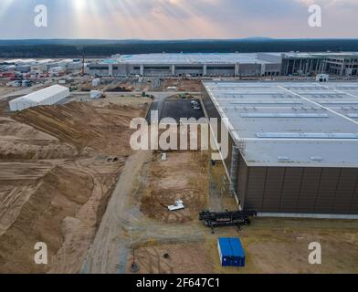 26. März 2021, Brandenburg, Grünheide: Die Baustelle des Tesla Gigafactory östlich von Berlin mit der Produktionshalle (Rückseite) und der Lackiererei (Vorderseite) (Luftaufnahme mit Drohne). Maximal 500.000 Fahrzeuge pro Jahr sollen ab Juli 2021 im Werk von der Produktionslinie Rollen - wobei der Automobilhersteller so schnell wie möglich das Maximum erreichen will. Der US-amerikanische Elektroauto-Hersteller erwartet vorerst, in seinem geplanten ersten Werk in Europa bis zu 10.500 Mitarbeiter im Schichtbetrieb beschäftigen zu können. Foto: Patrick Pleul/dpa-Zentralbild/ZB Stockfoto
