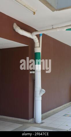 Nahaufnahme Downspout verbunden mit Regenrinne auf dem Dach, läuft durch die Decke entlang der Außenwand und führt Fliesenboden in unterirdischen Abfluss Stockfoto