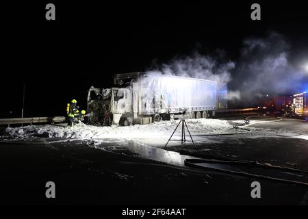 Eisenberg, Deutschland. März 2021, 30th. Feuerwehrleute löschen das Feuer auf einem LKW auf der Autobahn 9 in Richtung München. Die Zugmaschine des mit Holz beladenen Sattelzugwagens hatte Feuer gefangen. Das Feuer breitete sich auch auf den Sattelauflieger aus, der mit imprägniertem Gartenholz beladen war. Kredit: Bodo Schackow/dpa-zentralbild/dpa/Alamy Live Nachrichten Stockfoto