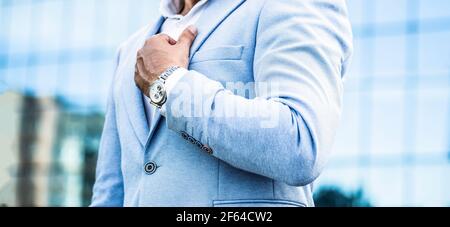 Schaut in einen Mann. Geschäftsmann zeigt auf seine Uhr im Hintergrund der Stadt. Der Mensch hält seine Uhr. Portrait erfolgreicher Geschäftsmann in einem Business-Anzug Stockfoto