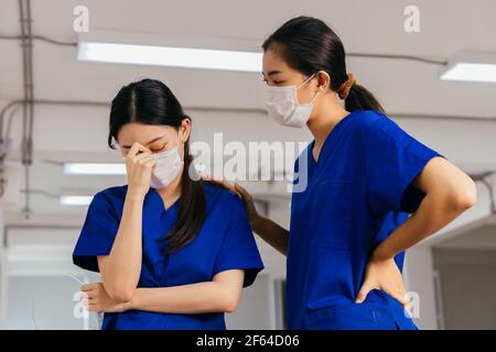 Gestresste Krankenschwester beruhigend frustriert und müde Mitarbeiter trägt Maske und Uniform während des Ausbruchs der Covid-19-Virus-Pandemie Stockfoto