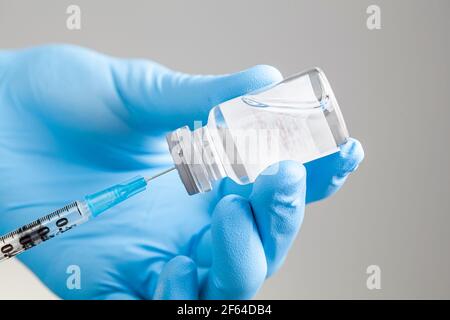 Nahaufnahme isoliertes Konzeptbild für einen Arzt, der flüssige Medikamente oder Impfstoffe aus einem Glasfläschchen mit Saugkappe in eine Spritze saugt. Stockfoto