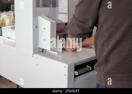 Der Arbeitsbediener arbeitet an einer automatischen Maschine zum Schneiden von Stapel von Papieren oder Etiketten, einem professionellen Schneidewerkzeug, Ausrüstung für eine Druckerei oder Werkstatt Stockfoto