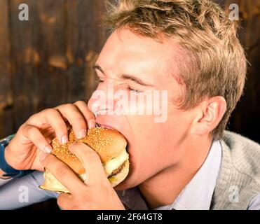 Schöner Mann, der Cheeseburger isst Stockfoto