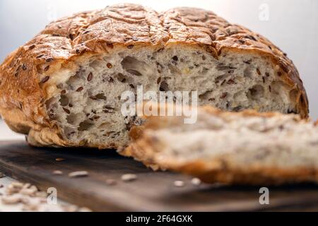 Close up Brotscheiben auf Servierbrett mit Flachs und Sonnenblumenkerne. Frisches, leckeres, rundes Weizenbrot mit Leinsamen auf einem weißen Strukturtisch mit s Stockfoto