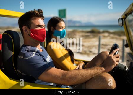 Glückliches kaukasisches Paar mit Gesichtsmasken, das im Strandbuggy sitzt Stockfoto