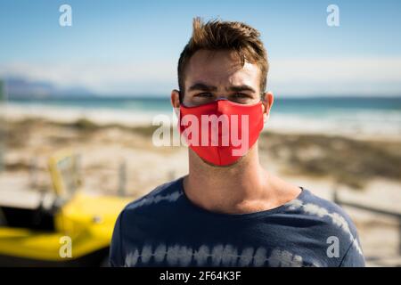 Porträt eines glücklichen kaukasischen Mannes mit Gesichtsmaske daneben Strandbuggy mit Blick auf die Kamera Stockfoto