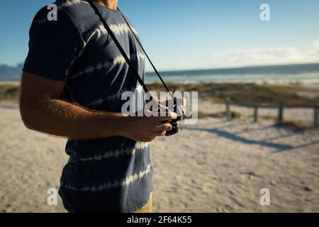 Mittelteil eines kaukasischen Mannes am Strand mit Kamera Stockfoto
