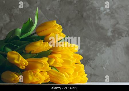 Bouquet von hellen gelben Tulpen auf weißen Holzoberfläche auf grauem Hintergrund liegend, kopieren Raum Stockfoto