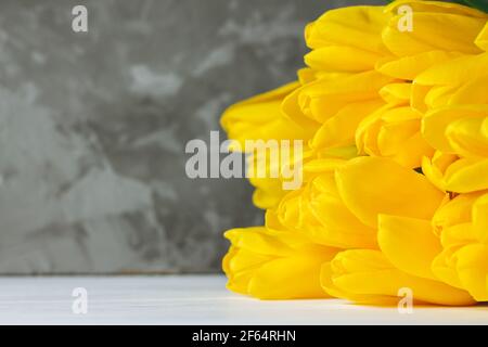 Bouquet von hellen gelben Tulpen auf weißen Holzoberfläche auf grauem Hintergrund liegend, kopieren Raum Stockfoto