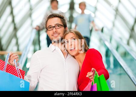 Ein Paar - Mann und Frau - in einem Einkaufszentrum Mit bunten Taschen auf einer Rolltreppe Stockfoto