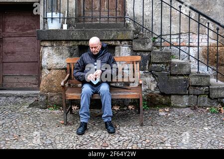 Ältere ältere Mann sitzt auf Bank & passt Gesichtsmaske, St. Nikolaus- und Marienfriedhof I, Prenzlauer Allee 1. Berlin Stockfoto