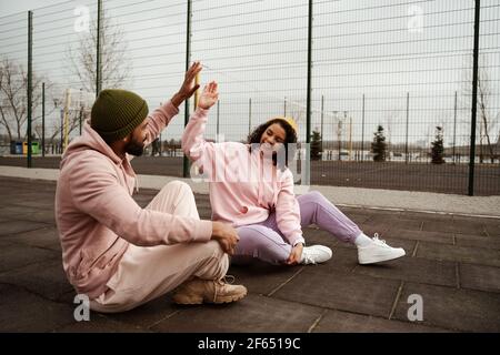 Aufgeregt afroamerikanische Freunde in Sportswear geben High fünf während Sitzen auf Sportplatz Stockfoto