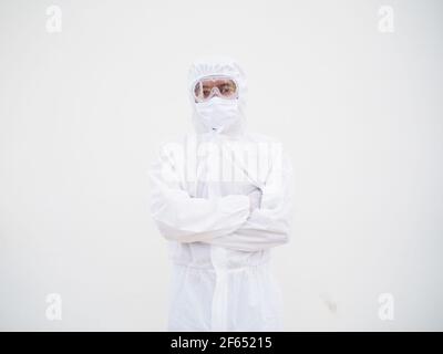 Porträt eines selbstbewussten asiatischen männlichen Arztes oder Wissenschaftlers in PSA-Uniform, während er seine Hände auf weißem Hintergrund faltet. Coronavirus oder COVID-19 con Stockfoto