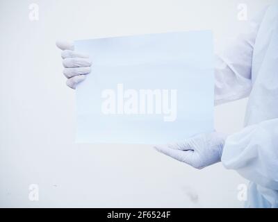 Nahaufnahme Hände des Arztes oder Wissenschaftlers in PSA-Uniform, die leeres Papier für Text mit beiden Händen halten, während sie nach vorne schauen. Coronavirus oder COVID-19 CO Stockfoto