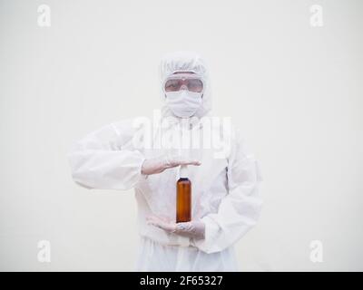 Porträt von Arzt oder Wissenschaftler in PSA-Suite Uniform halten Plastikflasche mit Hautpflegeprodukt. COVID-19 Concept isolierter weißer Hintergrund Stockfoto